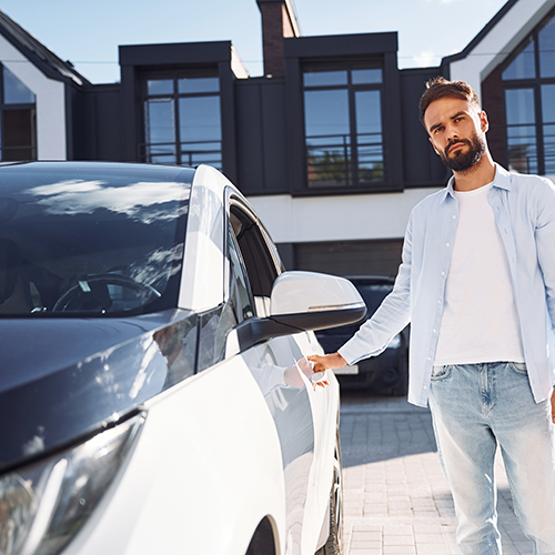 Seguros de hogar y coche representados por un hombre abriendo su coche en la entrada de casa.